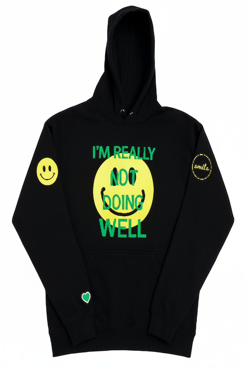 A black pullover hoodie with a graphic design on the front. The design features a large yellow smiley face with the text 'I'M REALLY NOT DOING WELL' in green.