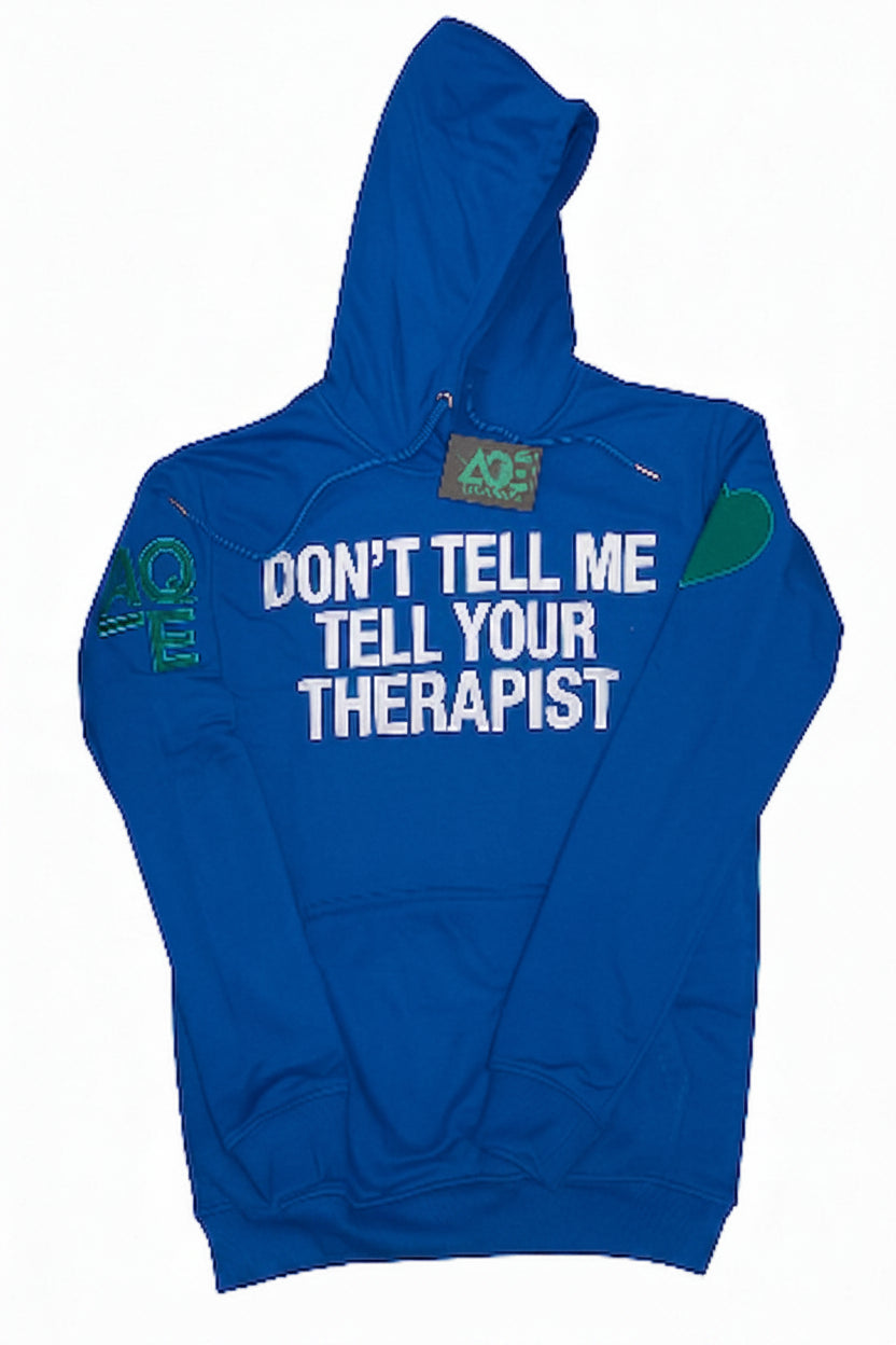 A blue pullover hoodie with a front kangaroo pocket, featuring white text that reads 'DON'T TELL ME TELL YOUR THERAPIST' across the chest, a green heart on the right sleeve, and green 'AQE text on the left sleeve.