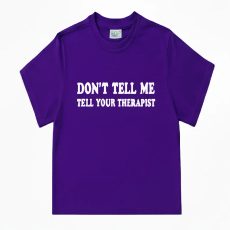 A purple short-sleeve crewneck t-shirt with the text 'DON'T TELL ME TELL YOUR THERAPIST' in white letters