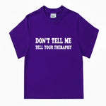 A purple short-sleeve crewneck t-shirt with the text 'DON'T TELL ME TELL YOUR THERAPIST' in white letters