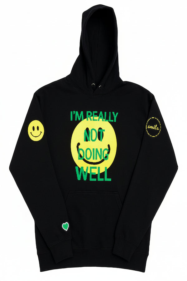 A black pullover hoodie with a graphic design on the front. The design features a large yellow smiley face with the text 'I'M REALLY NOT DOING WELL' in green.