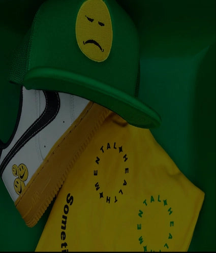 A green trucker hat with a yellow sad face patch.