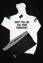 A white hooded sweatshirt with bold black text that reads 'DON'T TELL ME TELL YOUR THERAPIST' across the chest, a green heart on the right sleeve, and green 'AQE text on the left sleeve.