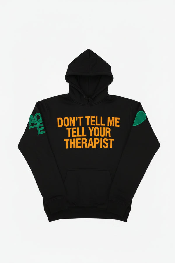 A black pullover hoodie with a front kangaroo pocket, featuring orange text that reads 'DON'T TELL ME TELL YOUR THERAPIST' across the chest, a green heart on the right sleeve in support, and green 'AQE" text on the left sleeve in support of mental health.
