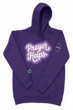 A purple pullover hoodie with 'Prayer Helps' printed in white script across the chest inside a wavy purple border. The hoodie also features a small green heart on the lower left front pocket and a small circular logo on the right sleeve.