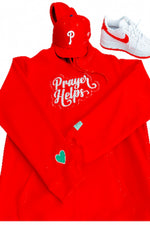 A red hoodie with 'Prayer Helps' in white script, a matching red baseball cap with a white 'P' logo, and a white Nike sneaker with red accents, arranged on a white background.